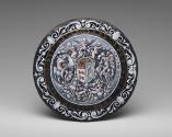 Back of black painted enamel dish depicting cherubic figures surrounding a coat of arms at the …