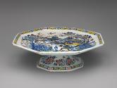 Side view of a footed platter with ornate floral and figurative decoration in color