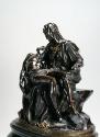 Side view of a bronze sculpture of a pietà scene.   The Madonna is seated with the deceased fig…