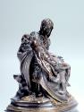 Side view of a bronze sculpture of a pietà scene.   The Madonna is seated with the deceased fig…