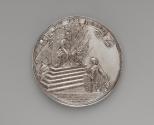 Silver medal depicting a crowned male on a throne offering a scepter wrapped in laurel to a kne…