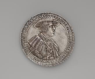 Silver medal of a man wearing a broad hat, pleated shirt, wide-collared cloak, and the badge of…