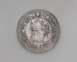 Silver medal of a man and woman holding hands, between whom a dove descends with an olive branc…