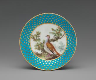 Porcelain saucer in blue and gold with image of bird near tree