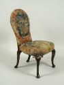 Chair with needlepoint upholstery showing woman seated outside, birds, flowers, and vegetal dec…