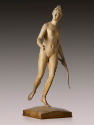 A terracotta sculpture of Diana.   She stands on the ball of her left foot, her right foot is e…