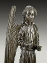 Close up view of a bronze sculpture of an angel.  The angel stands upright, with wings stretche…
