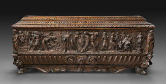 Front view of chest with high relief carving and coat of arms in the center