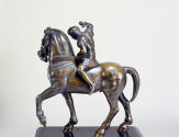 Back view of bronze sculpture of a warrior on horseback.  The warrior figure has his right arm …