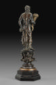 Back view of a bronze sculpture of a female figure with a cornucopia.  Her head is turned to he…