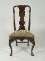 Front view of walnut frame chair with needlepoint upholstered seat with woman standing outdoors