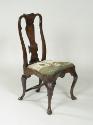 Walnut frame chair with needlepoint upholstered seat with woman standing outdoors