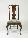 Front view of walnut frame chair with needlepoint upholstered seat with woman standing outdoors