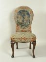 Chair with needlepoint upholstery showing man and woman outside with tree, with vegetal decorat…