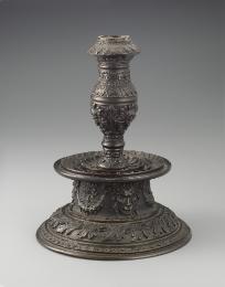 Bronze candlestick featuring intricate motifs throughout.