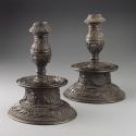 View of the pair of bronze candlesticks featuring intricate motifs throughout.